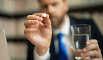 Close up portrait of man taking a medicine pill from headache migraine. Hand with medicine pill selective focus. Headache and eye strain on laptop. Business man with stress and fatigue eyestrain.