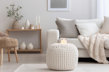 Modern living room interior featuring a knitted pouf, white fabric sofa, blanket, and terra cotta pillows. The comfort and style of Hygge and Scandinavian design, creating a cozy and stylish space.