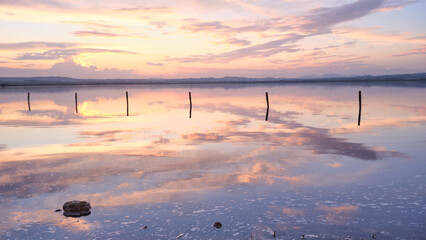 Sunset on the salt lagoon with reflections of clouds and silhouettes of reflections