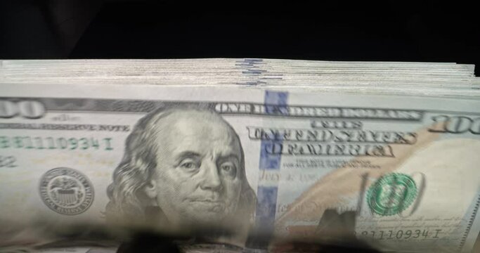 Closeup of hundred dollar bill banknotes flipping through in counting machine. Black background. Banking finance business investment stocks, financial growth, financial literacy, wealth and security