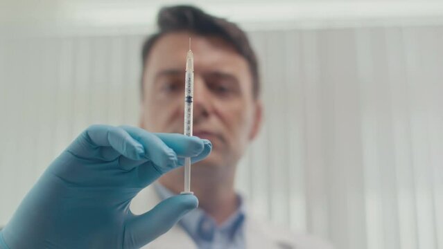 Focus on syringe with collagen treatment prepared by male doctor in medical gloves for patient