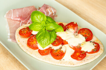 Flatbread with cherry tomatoes, mozzarella, basil leaves and fresh prosciutto on a rectangular plate