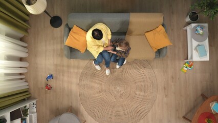Top view of grandmother in casual clothing with little boy sitting on the sofa in the living room, holding hands.