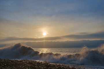 Waves on the rocky beach with cloudy sunset sky background
