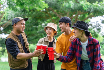 Happy asian diverse group friends enjoy drinking a beer together. They feeling relaxed and refreshing while camping in the nature. Recreation and journey outdoor activity lifestyle.