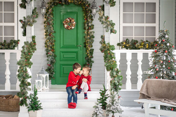 Obraz na płótnie Canvas Two children girl and boy playing at Christmas veranda decorations. Street christmas decor with artificial snow.