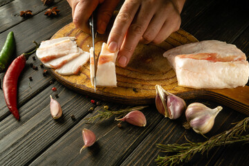 The chef cuts pork lard with a knife on a wooden cutting board. Concept of delicious peasant food...
