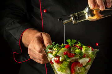 The cook adds olive oil to a vitamin salad for lunch. The concept of preparing a vegetarian dish with the hands of a chef. Vegetable dish in a bowl