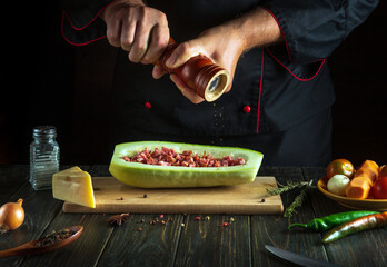 Cooking the national dish boat from minced meat and zucchini. Adding pepper using a mill in the hands of a cook