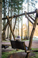 woman sitting on swings in the middle of the forest in cold winter time, warm clothes 