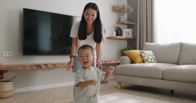 Mom and baby playing together at home. Asian multiethnic mom and son running around house in living room playing catch-up, having fun, spending time together with fun, laughing, smiling, enjoying game