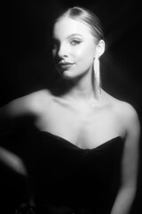 Make-up and fashion concept. Beautiful classic woman portrait. Model with classic hairstyle, fancy earrings, black dress. Shiny star filter applied. Model looking at camera. Black and white image