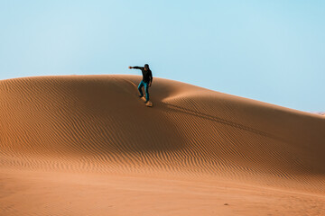 Man sliding down with a sand board in a dune in the Sultanate of Oman.