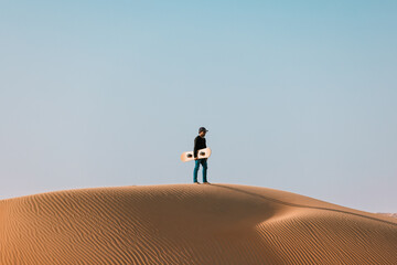 Stock photo of a man standing on top of a dune with his sand board. 