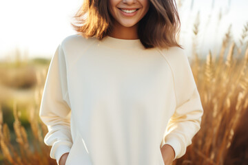 Young blond woman wearing blank white, cream or beige sweatshirt stands in front of camera. Fashion mockup with copy space. Sweatshirt template. Generative AI - obrazy, fototapety, plakaty