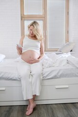 A pregnant blonde woman takes pictures of her belly. Pregnancy, smartphone use. A pregnant woman uses a pregnancy app

