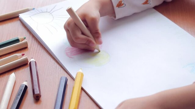 A preschool child draws with colored pencils in an album. Child's hand with a pencil close-up, selective focus. The girl draws a colored cloud