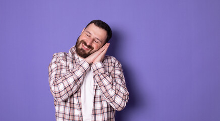 Handsome bearded man over purple background sleeping dreaming and posing with hands together while smiling with closed eyes.