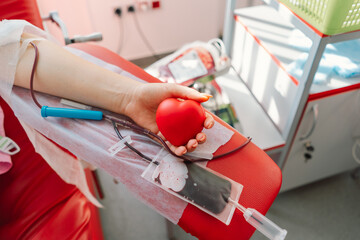 Young woman making blood donation in hospital. A woman donates blood while holding a red heart....