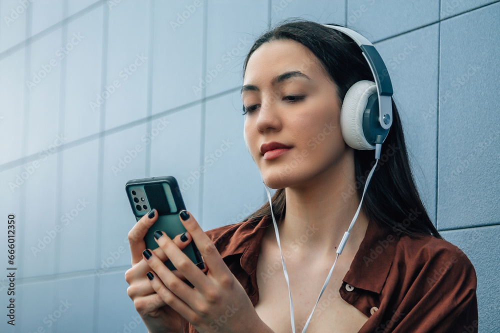 Wall mural relaxed young woman with headphones and phone on blue wall