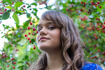 Pretty girl smiling while taking photo in cherry garden. Portrait of young girl with makeup. Ripe cherry fruits in the background. Representing summer season season and vitamins, healthy natural life