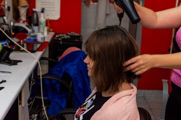 Portrait of young girl in hair salon while female hairdresser is drying her hair