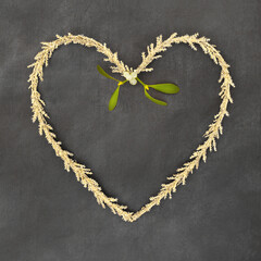 Christmas gold tinsel heart shape wreath with mistletoe sprig. Traditional romantic symbol for the festive holiday season on grunge gray background. 