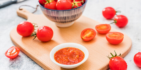 Cherry tomatoes and tomato sauce placed on the cutting board