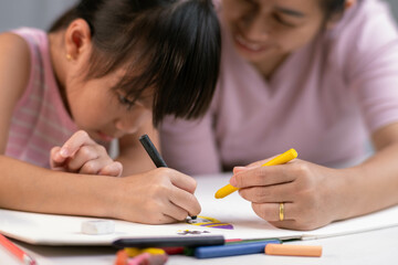Mother and daughter drawing together with crayons. Adult woman helps girl study or draw together at...