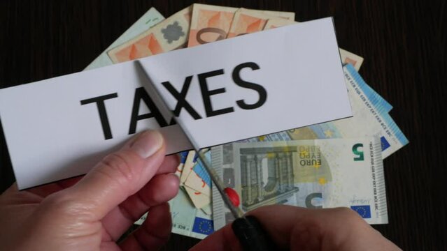 the cutting paper with inscription taxes lies on top of a large pile of euro money on a dark wooden table, top view, tax reduction