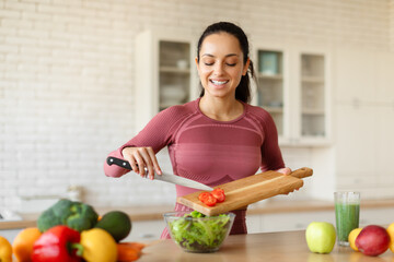 Happy fit woman cooking healthy vegetable salad in kitchen interior