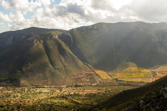 Dreamy landscape with subtle sun rays iluminating the plateau of Leonidio while dark clouds are gathering over the green mountains.