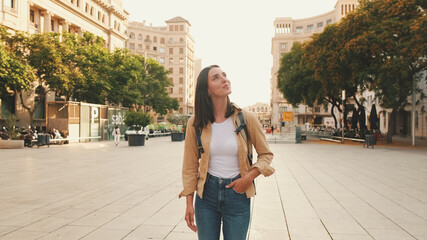 Traveler girl, with backpack on her shoulders, walks in the historical part of European city - obrazy, fototapety, plakaty