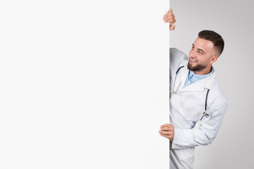 Doctor peeking from behind blank white board