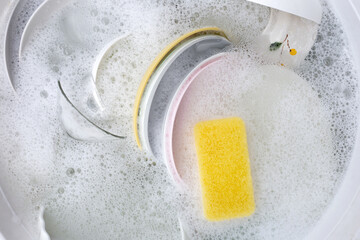 Dishes and bowls in water and bubbles of dishwashing liquid. Kitchen work