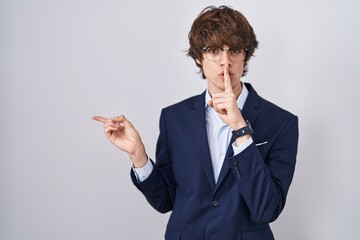 Hispanic business young man wearing glasses asking to be quiet with finger on lips pointing with...