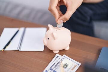Young blond man inserting coin on piggy bank at home