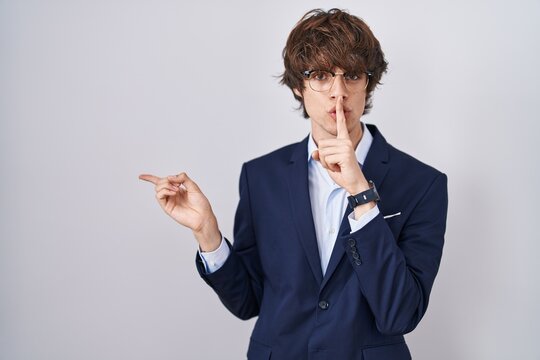 Hispanic business young man wearing glasses asking to be quiet with finger on lips pointing with hand to the side. silence and secret concept.