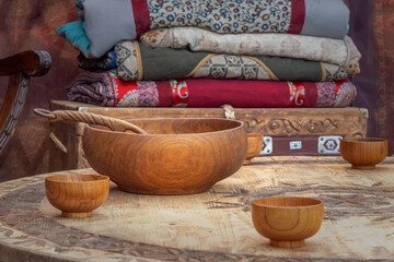 Traditional Asian wooden utensils for milk drinks stand on a low table against the background of a chest with blankets inside a nomadic home - a yurt. Close-up