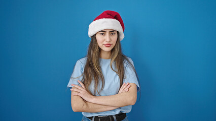 Young beautiful hispanic woman standing upset wearing christmas hat over isolated blue background