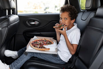 Hungry african american boy eating pizza while riding car