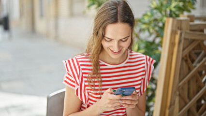 Young blonde woman using smartphone smiling at coffee shop terrace