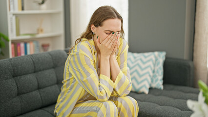 Young blonde woman stressed sitting on sofa crying at home