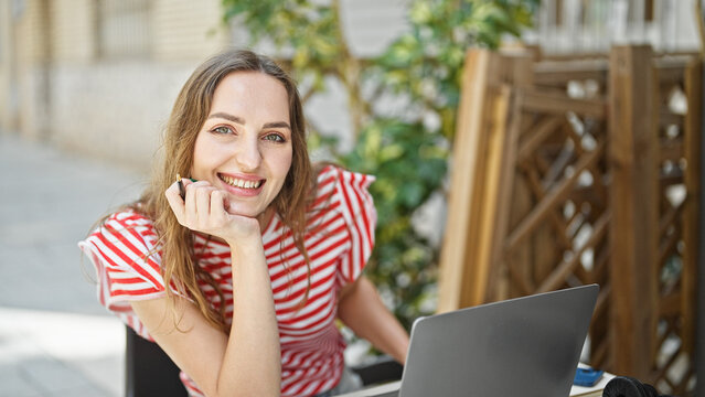Young blonde woman using laptop sitting on table at coffee shop terrace