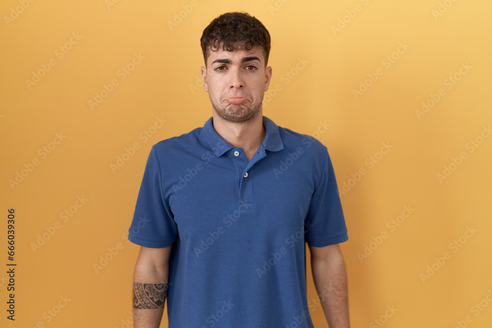 Sticker young hispanic man standing over yellow background depressed and worry for distress, crying angry an