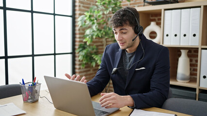 Fototapeta na wymiar Young hispanic man business worker using laptop wearing headset at office