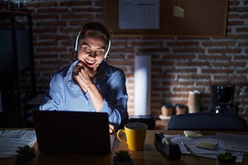Beautiful brunette woman working at the office at night looking confident at the camera smiling with crossed arms and hand raised on chin. thinking positive.
