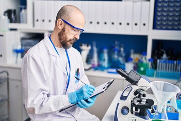 Young bald man scientist writing report working at laboratory