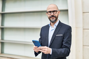 Young bald man business worker smiling confident using smartphone at street