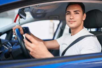 Obraz premium Young hispanic man using smartphone sitting on car at street